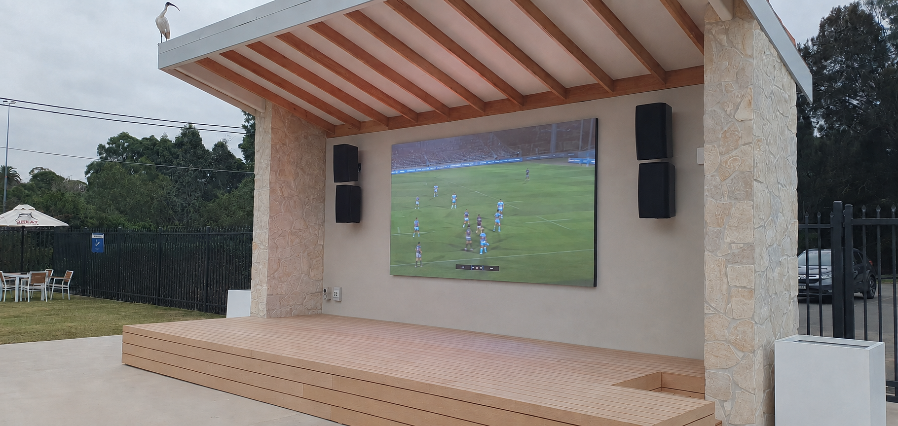 The finished outdoor courtyard LED screen at The Concord Club, showing a live sports broadcast under a covered stage.