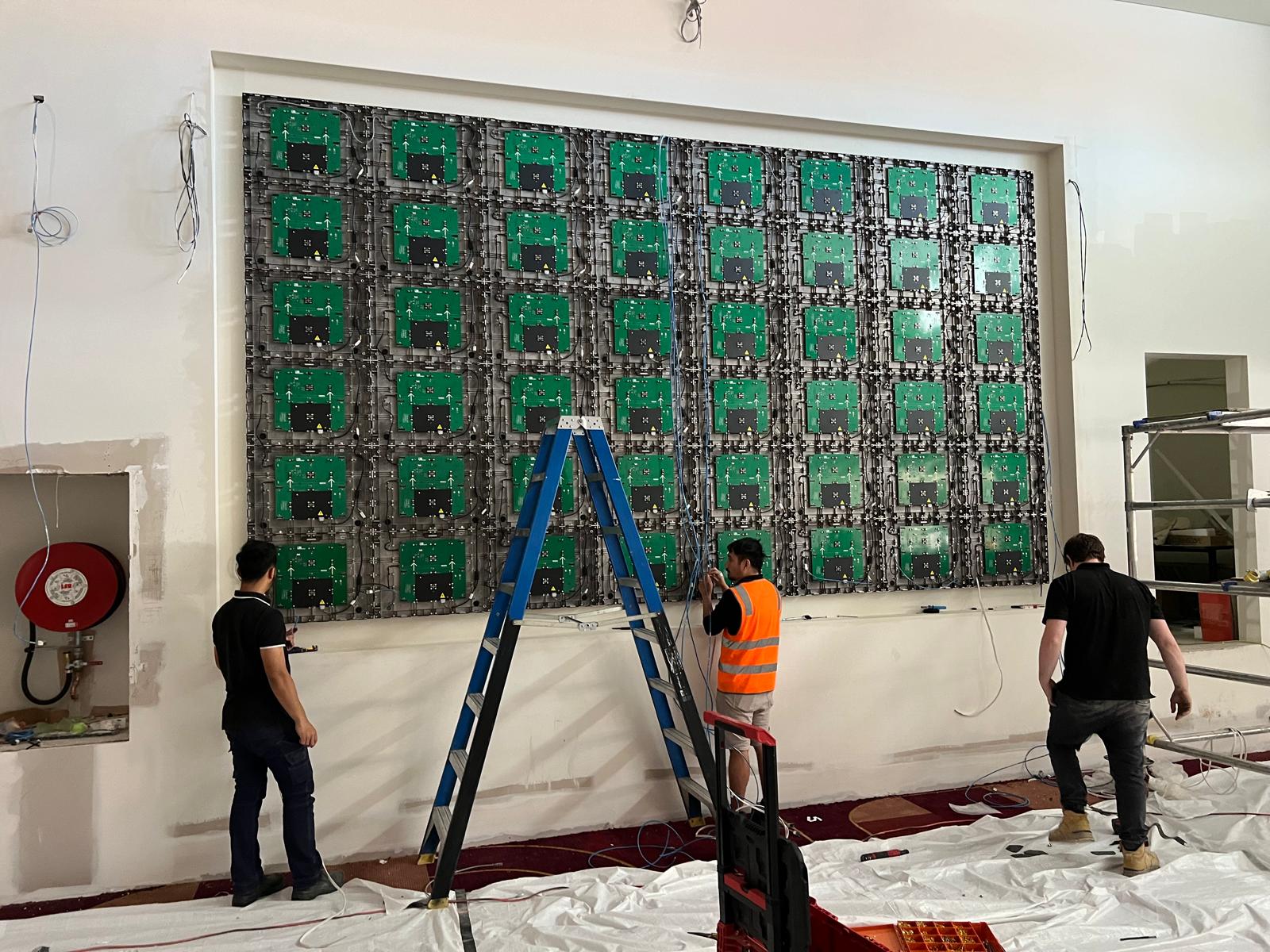 Further LED module installation on the sports bar wall, with the module grid partially complete.