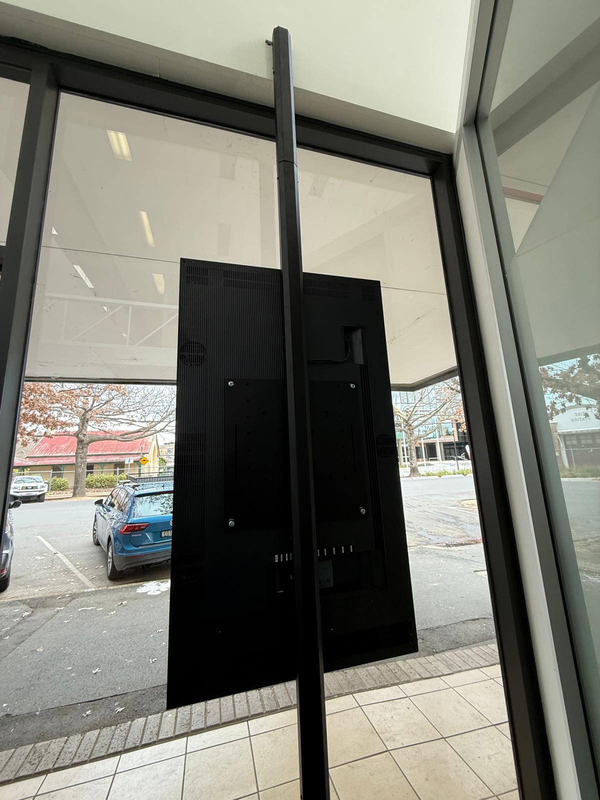 Rear close-up showing the vertical mounting structure, display fixing method and cable management behind the floor-to-ceiling digital signage installation.