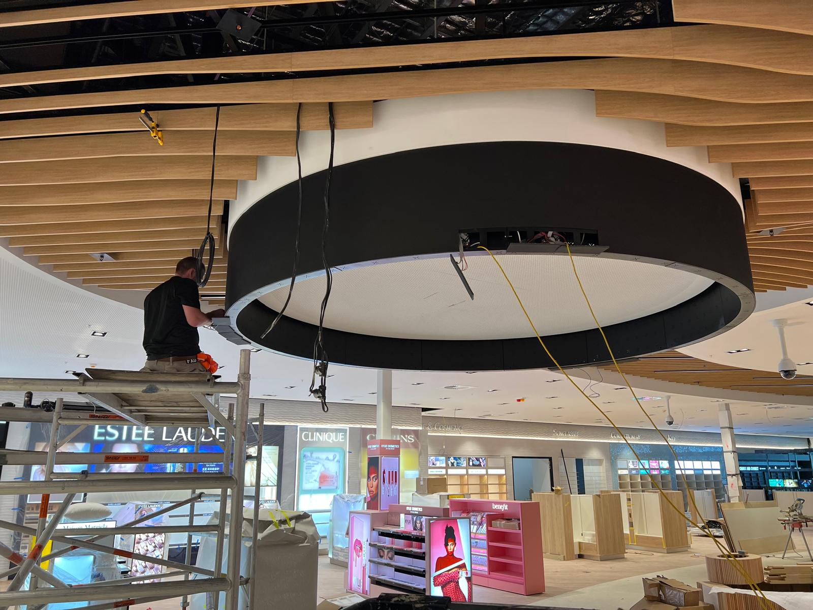 The halo display flush-mounted within the finished timber-slat ceiling, final touches underway before power-on.
