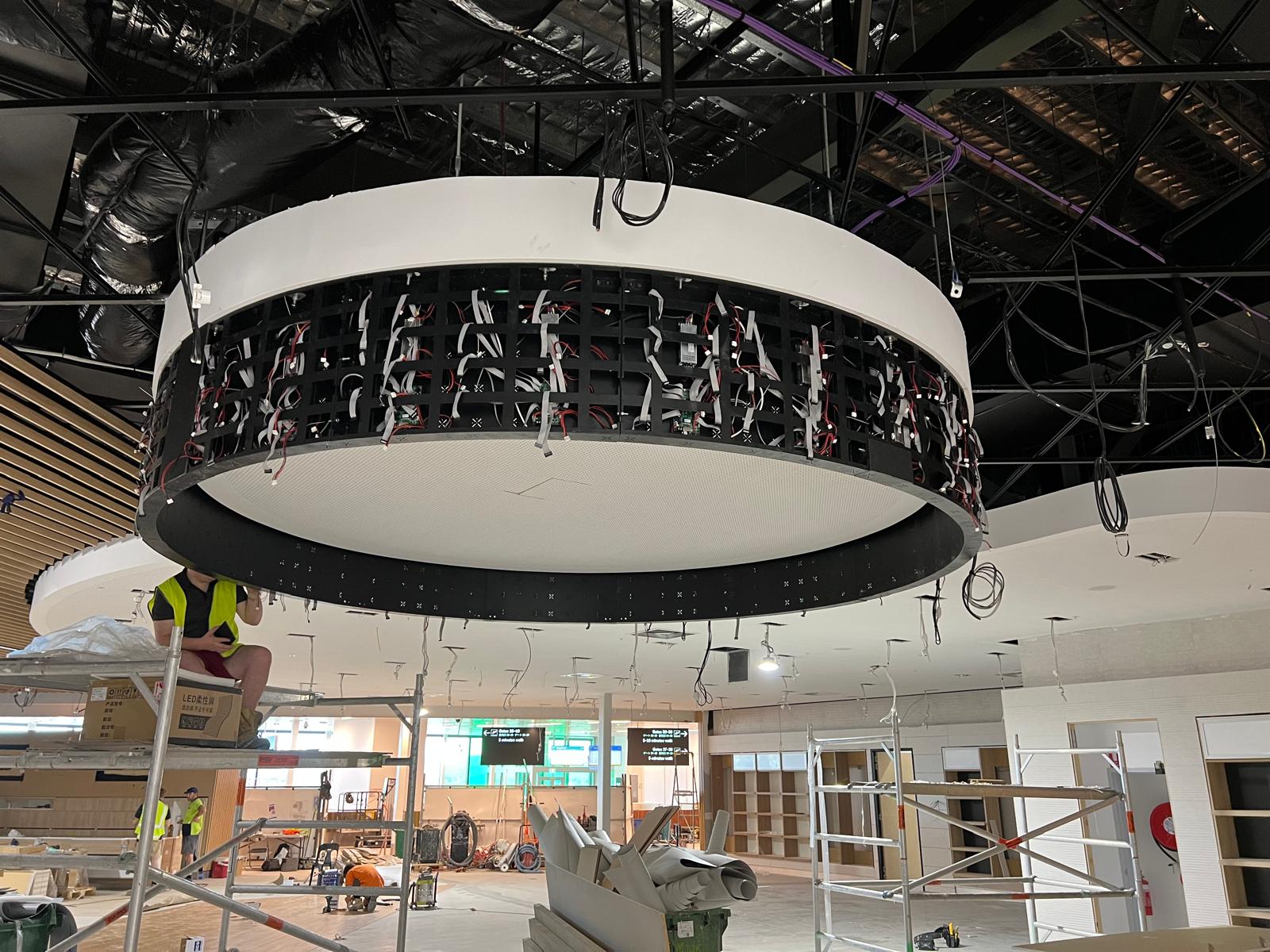 Wider view of the halo LED ring being wired into place, with airport gate signage visible in the background.