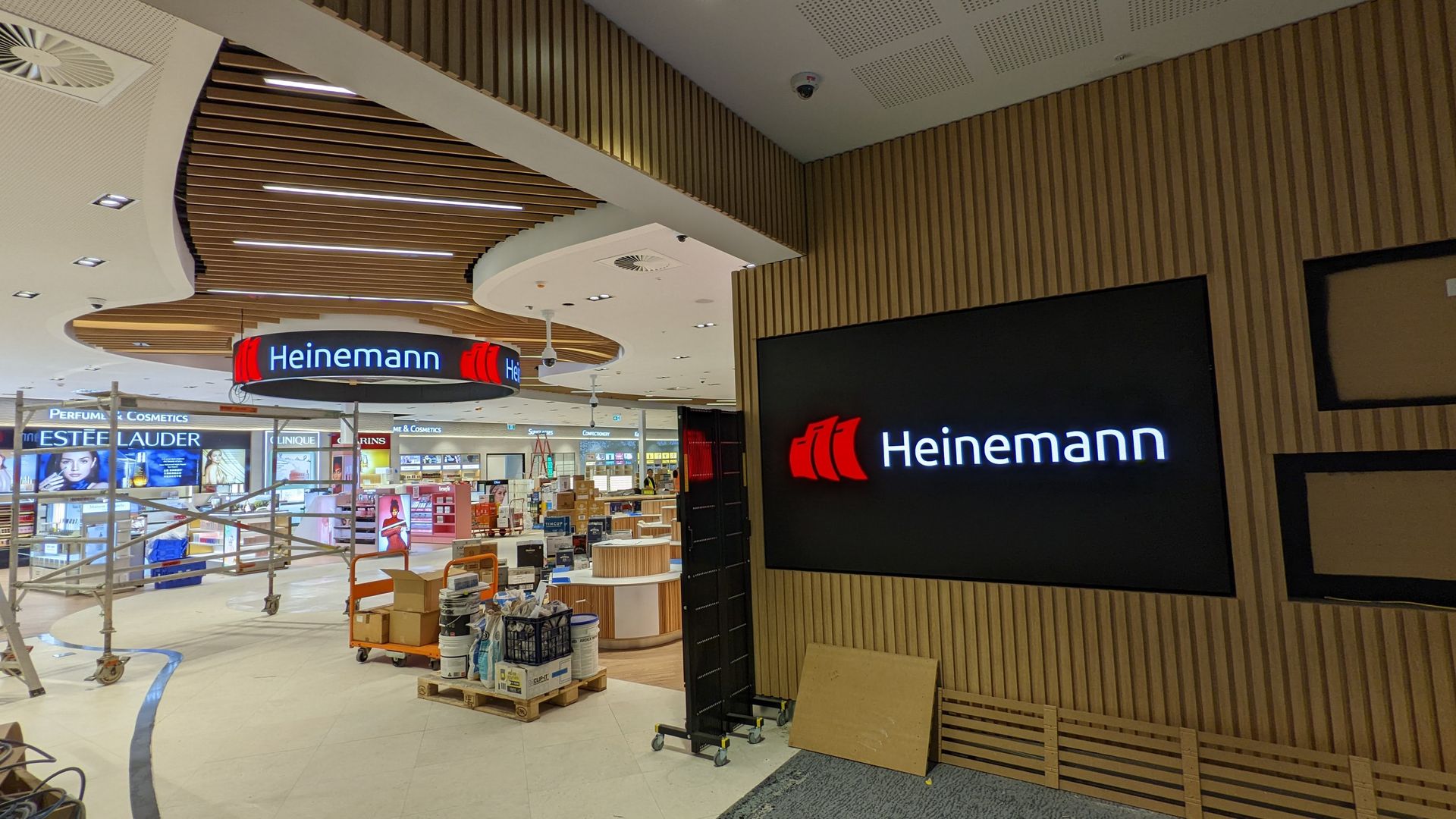 Wall-mounted LED display panel showing the Heinemann logo, installed amid ongoing shopfitting works.