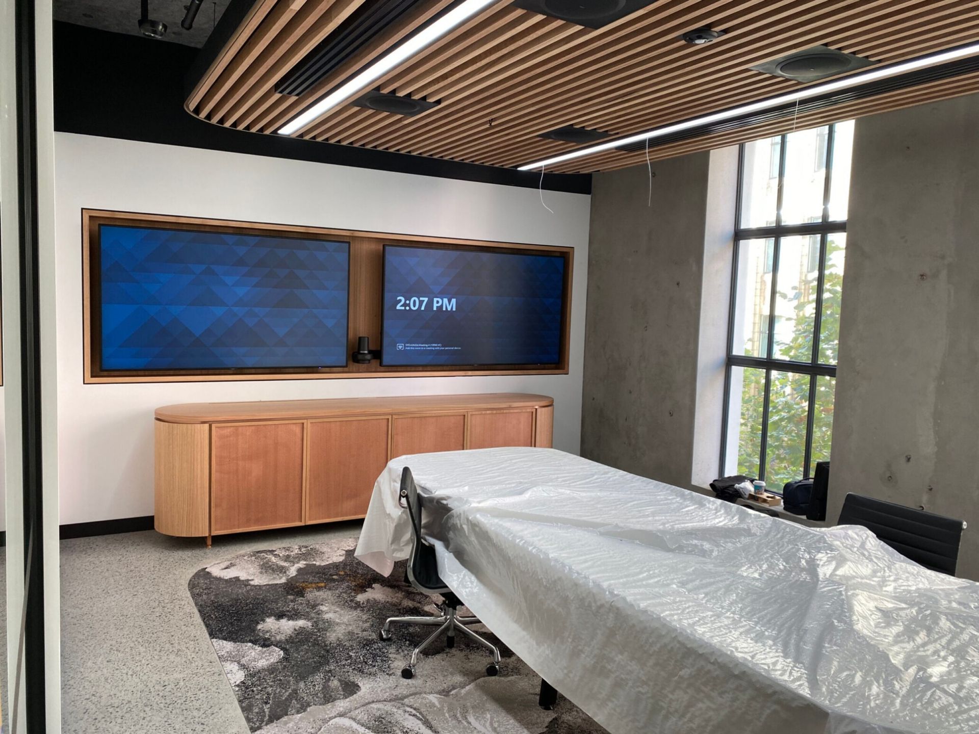 Dual-display boardroom AV installation, shown mid-fitout with the room's furniture still protected.
